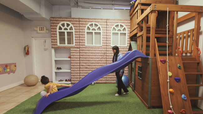 teacher and boy playing on a slide at Koala ABA Lerning Center, the best aba center in Florida